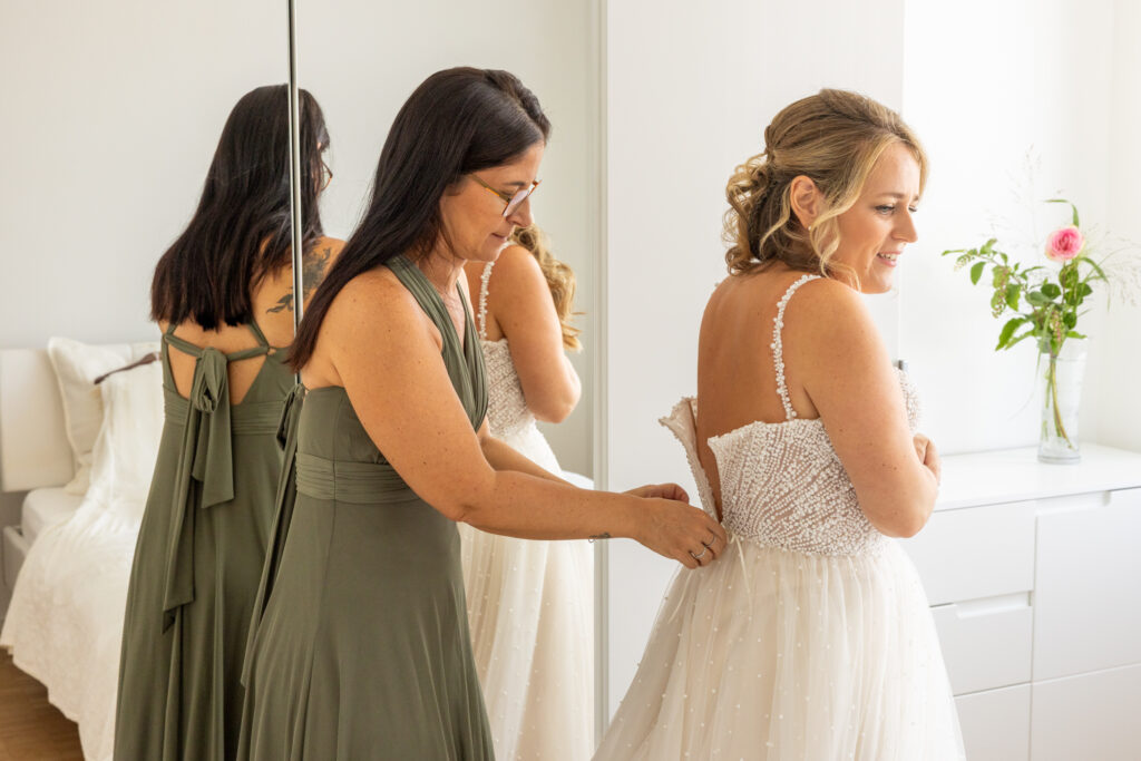 Trauzeugin hilft der Braut beim Anziehen des Hochzeitskleids